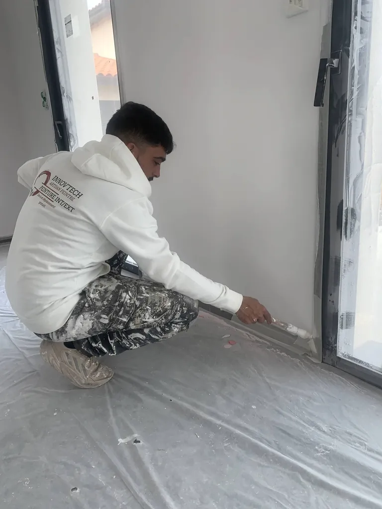 Peintre réalisant la finition d'une plinthe au pinceau