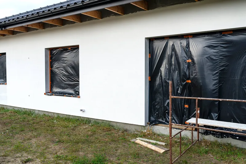 Façade de villa repeinte en blanc, fenêtres bâchées